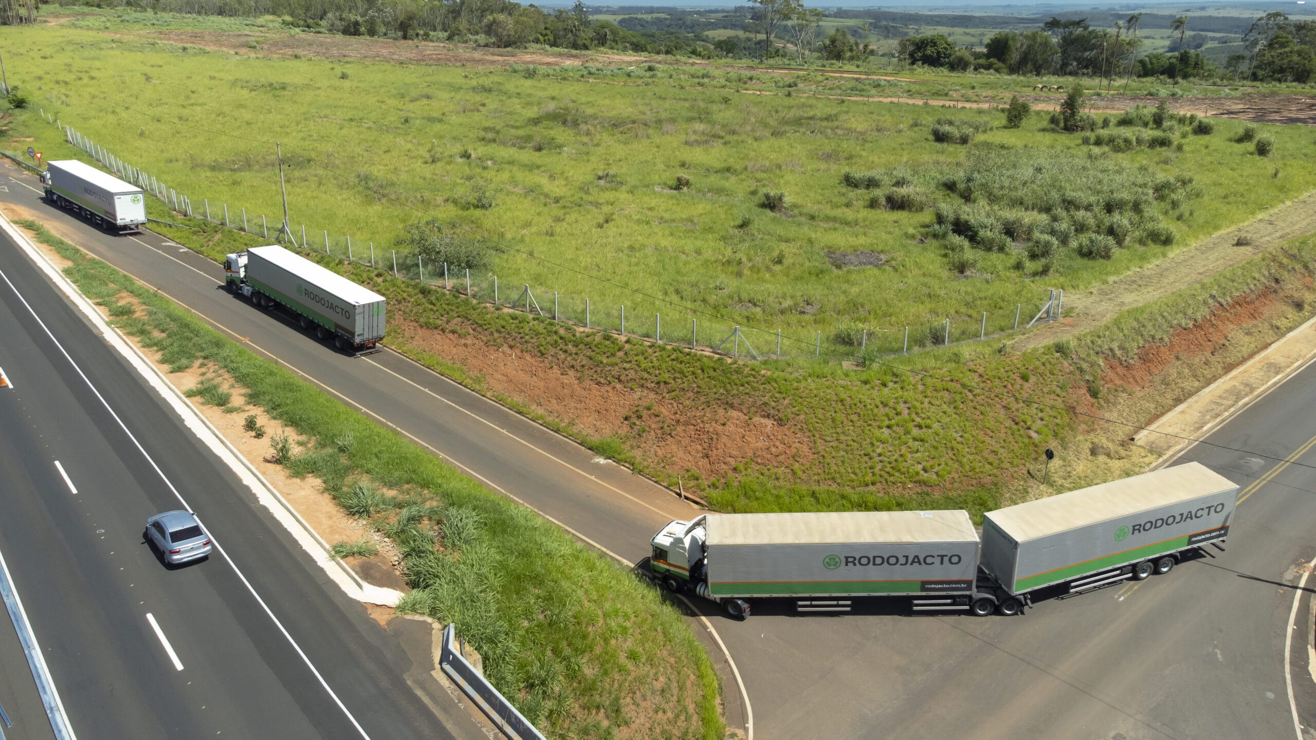 Como a Rodojacto usa a legislação no transporte de cargas? Caminhões Rodojacto de transporte de carga na rodovia, com área de vegetação verde ao fundo, destacando a importância do transporte rodoviário de cargas no Brasil e da legislação no transporte de cargas.